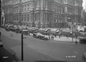 A photograph from April 26, 1918 depicting a supply convoy of military supply trucks outside city hall.
