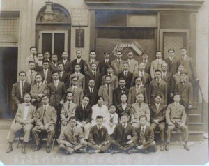 black and white photo of a group of about 45 men, two women, and a child seated in a pose in front of the First Chinese Baptist Church, Chinatown, Philadelphia. probably in the early 20th century.