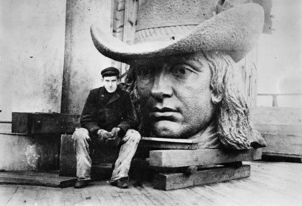 A black and white photograph of Alexander Milne Calder sitting in front of the bronze head of William Penn.