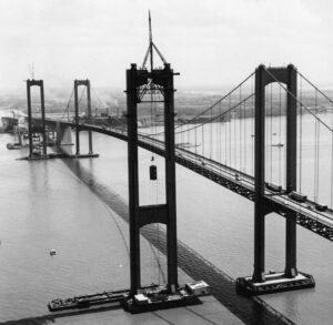 Two towers (spans) of bridge, with one of them being under construction. Cars drive along the completed span.
