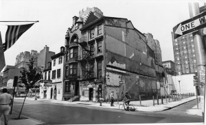 Photo en noir et blanc d'un bloc d'immeubles sur Locust Street. L'image montre quatre bâtiments au premier plan, avec des bâtiments plus élevés à l'arrière-plan. Il y a des gens debout et à vélo sur la rue devant les bâtiments.