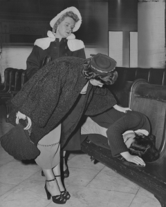 A black and white image of two female police officers wearing jackets leaning over a sleeping teenager on a bench. 