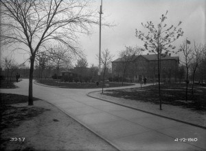 A black and white photograph of a he central garden of a park. Pathways lead to and from the central garden, and tress line the pathways. 