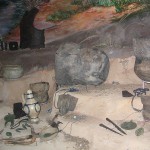 A color photograph of a variety of clay pots, jewelry, stone tools, metal tools, and other metal items are on an uneven brown landscape.