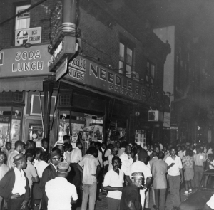 A black and white photograph of a large group of people standing next to a building. 