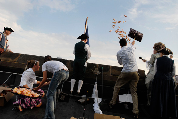 A photograph of actors dressed as French Revolutionairies and pop culture characters, throwing tastykakes over a wall with shovels