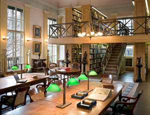 A color photograph of a reading room, with tables, lights, and bookshelves lining the walls. 