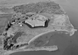 a black and white aerial photograph of a building in the middle of an island. 