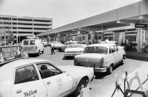 A black and white photograph of taxis and cars in front of an air port terminal. 