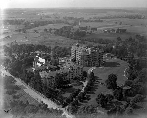 A black and white aerial photograph of three large, multi-story buildings in the middle of a tree grove.