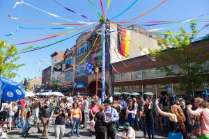 Color photograph of a crowd gatehred on South Street, celebrating around a maypole with colorful streamers on top