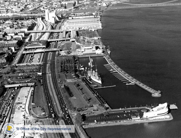 Black & white aerial photo of Penn's Landing waterfront, showing the harbor at Spruce Street, with USS Olympia at pier.