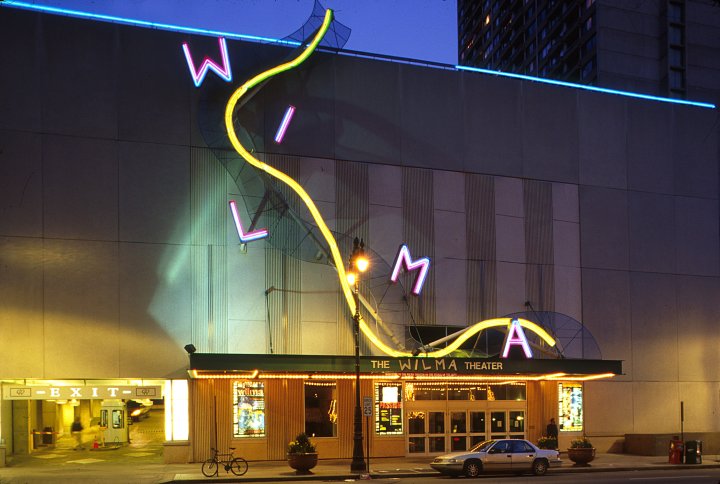 A color photograph of the Wilma Theatre at night, showing the neon facade
