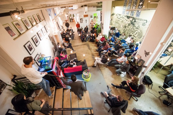 color photograph of large space at Indy Hall co-working with about three dozen people gathered in informal meeting.