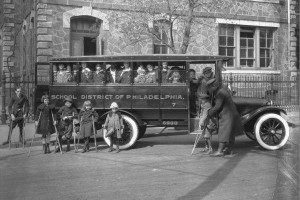 A black and white photo depicting children with disabilities boarding a school bus in 1923.