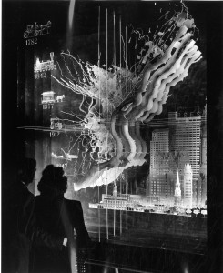 black and white photo with two silhouettes in left foreground looking at an exhibit using transparent maps of the city to illustrate the city's growth from 1782 to 1947.