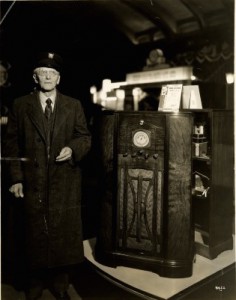 Black and white photograph of an older gentleman standing next to a large RCA Victor radio.