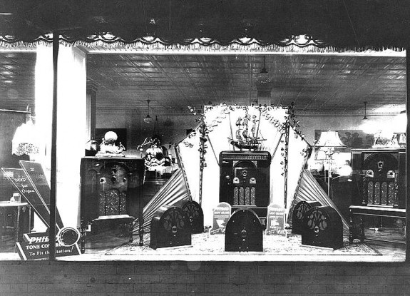 Black and white photo depicting a department store window display with several different models of Philco radios.