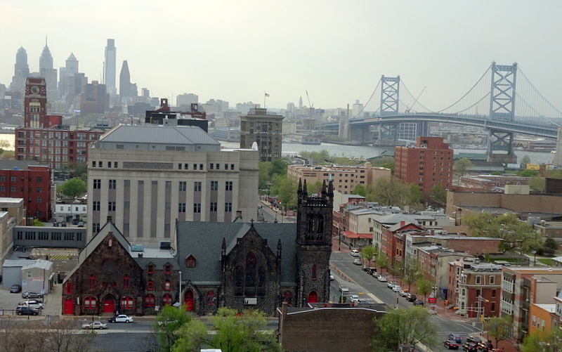 photograph of Camden in foreground with Ben Franklin Bridge and Rutgers-Camden campus at right and Philadelphia skyline rising in distance across Delaware River