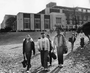 Black and white photograph depicting several young men walking away from a large school building.