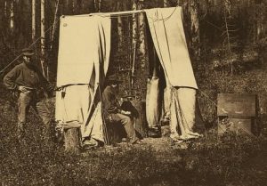 A photograph of an observatory tent with a man operating a theodolite.