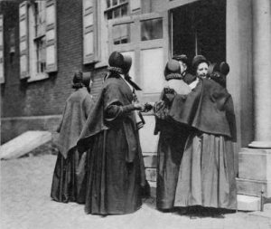 A black and white photograph of a group of Quaker women in traditional plain dress outside of a Meeting House
