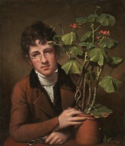 A portrait of Raphaelle's brother, Rubens Peale, seated at a wooden table, head angled slightly, with his hand around the clay pot of a large, green geranium plant with thick stalks and small red flowers. Rubens holds a pair of glasses on the table with his other hand, while wearing a pair of smaller diameter spectacles midway up his nose. He wears a reddish-brown coat and white scarf and undershirt. His hair is brown and the background is a slightly amber tannish-brown tone.