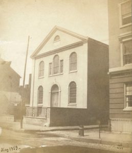 Sepia-toned photograph of the front of the two-story church building with arched windows and an arched doorway.