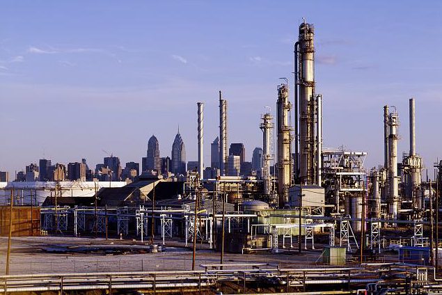 Full color photograph of oil refineries, center city can be seen in the background.