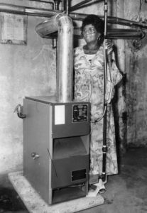 A woman stands next to her home heating system that is fueled by gas 