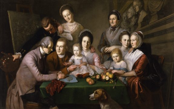 An image depicting Charles Willson Peale's family and children seated around a table, some standing, others seated. A peeled apple sits symbolically on a plate near the front of the table. His brothers work on a drawing of his mother, seated opposite them, several busts are located on a shelf at the top right, and a painting of the three maidens is to the left.