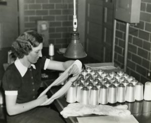 Black and white photograph of a woman inspecting nylon yarn with several spools of yarn sitting on a table in front of her.