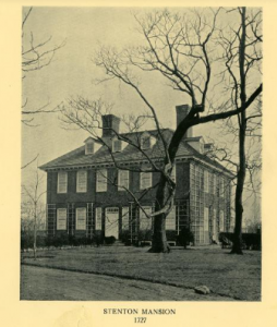 A black and white photograph of a Georgian-style mansion with a large, bare tree in front of it.