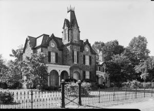 A black and white photograph of a Gothic Revival style mansion with a prominent central tower