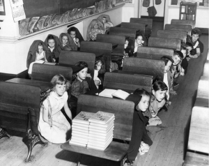 A black and white photograph showing a class room with children crouching under the desks during a 