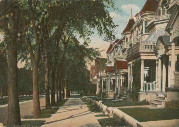A color postcard of a row of identical victorian row homes on a tree lined street