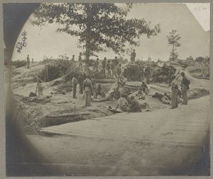 A black and white photograph of a group of African American soldiers sitting and standing in and around trenches