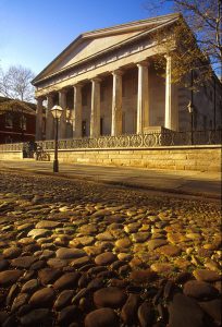 A color photograph of the Second Bank of the United States, a Greek Revival building resembling a temple with a cobblestone road in front of it.