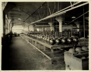 A black and white photograph of steel helmets being made on the assembly line of the Ford Automotive factory in 1917