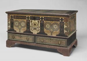 A color photograph of a black chest with colorful painted heart and flower motifs. The name "Magdalena Leabelsperger" and the year 1792 are painted on the top. 