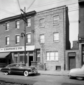 a black and white photograph of a three-story brick building with a sign reading "Sarcone & Son" on the front