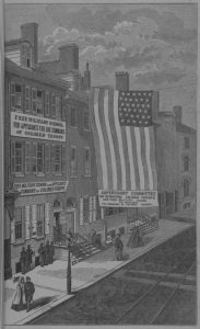 a black and white illustration of the Free Military School for Applicants for Command Command of Colored Troops, held in a large row house. An enormous american flag hangs from the roof to nearly street level near the front entrance.