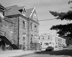 a black and white photograph of a three story stone convent with a cross topping the front-facing roof gable. A set of prominent stone stairs leads to the first floor entrance.