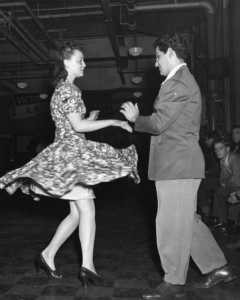 a black and white photograph of a couple performing the jitterbug. The woman has just executed a spin move and her skirt flares out from the movement.