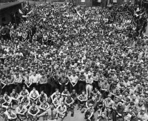 A black and white photograph of a crowd of thousands of men. The front row is seated while the rest stand.