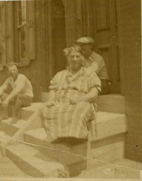 a black and white photograph of Maria Innocenza Procopio Siciliano and two unidentified men sitting on the stoop of a rowhouse
