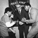 Joe Frazier poses with his fist raised opposite of PAL kids. In the background of the photograph is Police Commissioner Joseph O'Neill.