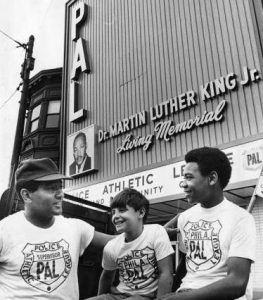 A PAL officer hangs out with two PAL children in front of a PAL building.