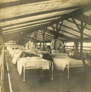 a black and white photograph of a doctor and nurse standing in a tent hospital full of beds.