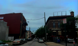 a color photograph of two brick buildings across the street from one another. The building on the right side of the street has signage reading "philadanco".